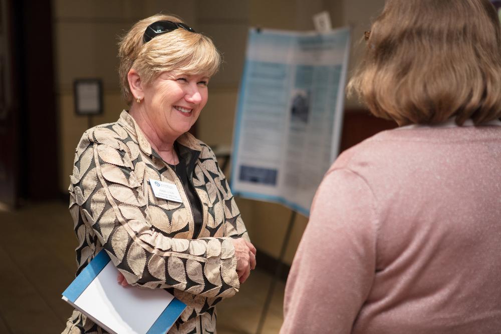 Faculty member with a name tag smiling at someone at the Graduate Showcase